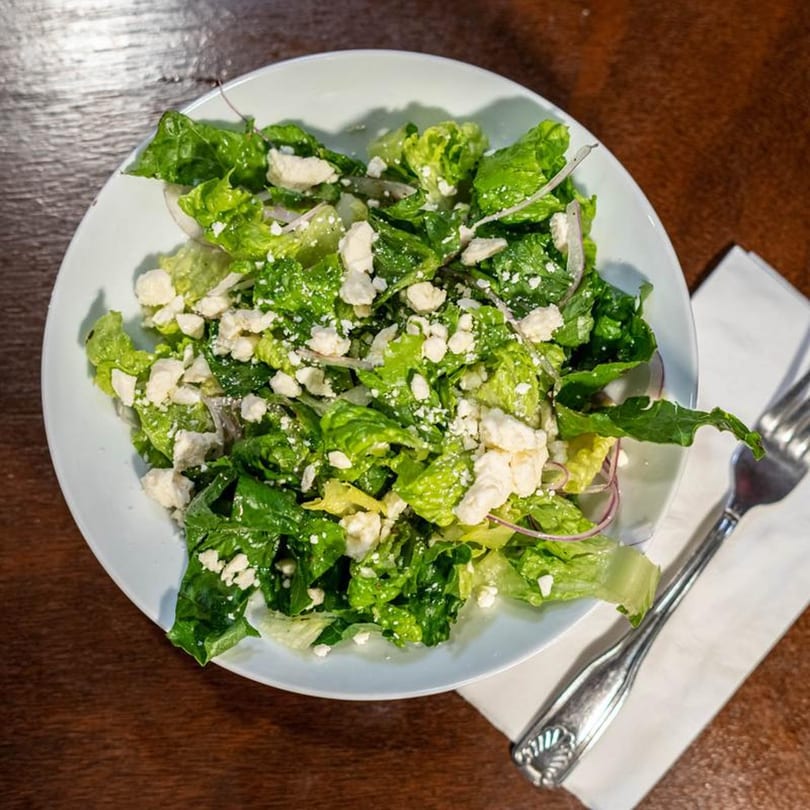 Fresh green salad with crumbled feta cheese and red onion, served in a white bowl.