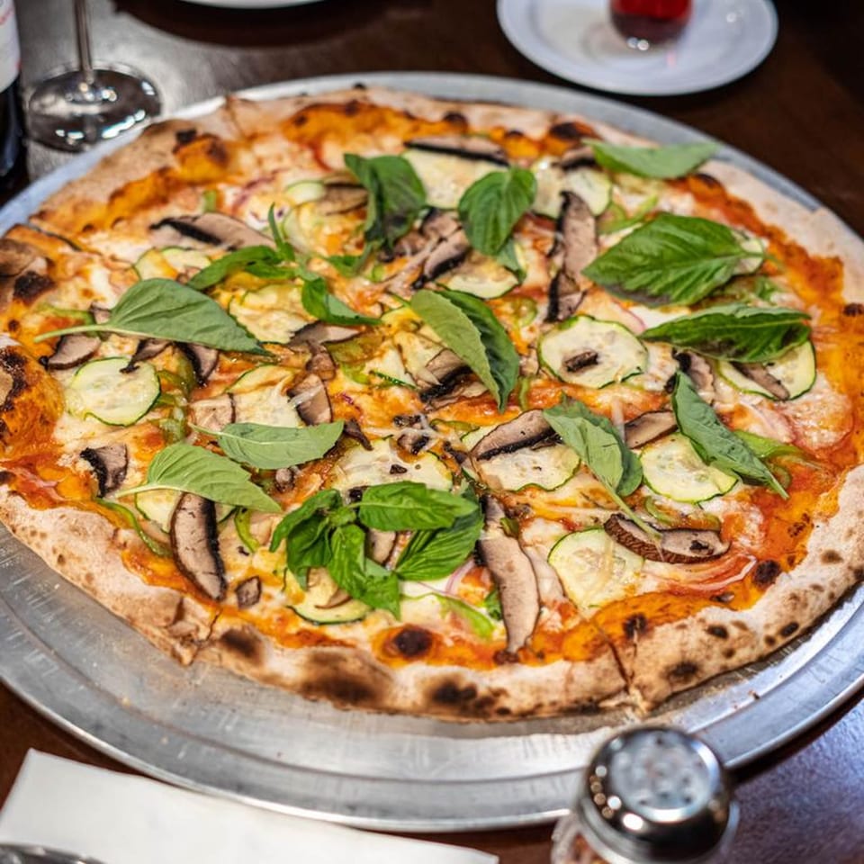 A Naudi Signature Pizza with mushrooms, zucchini, and basil on a metal tray.