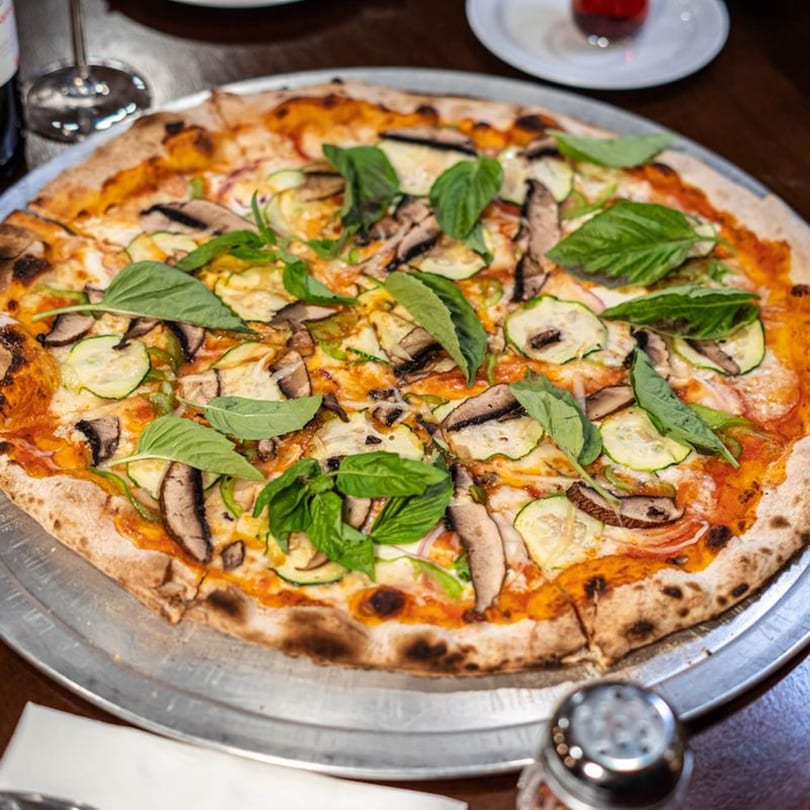 A Naudi Signature Pizza with mushrooms, zucchini, and basil on a metal tray.